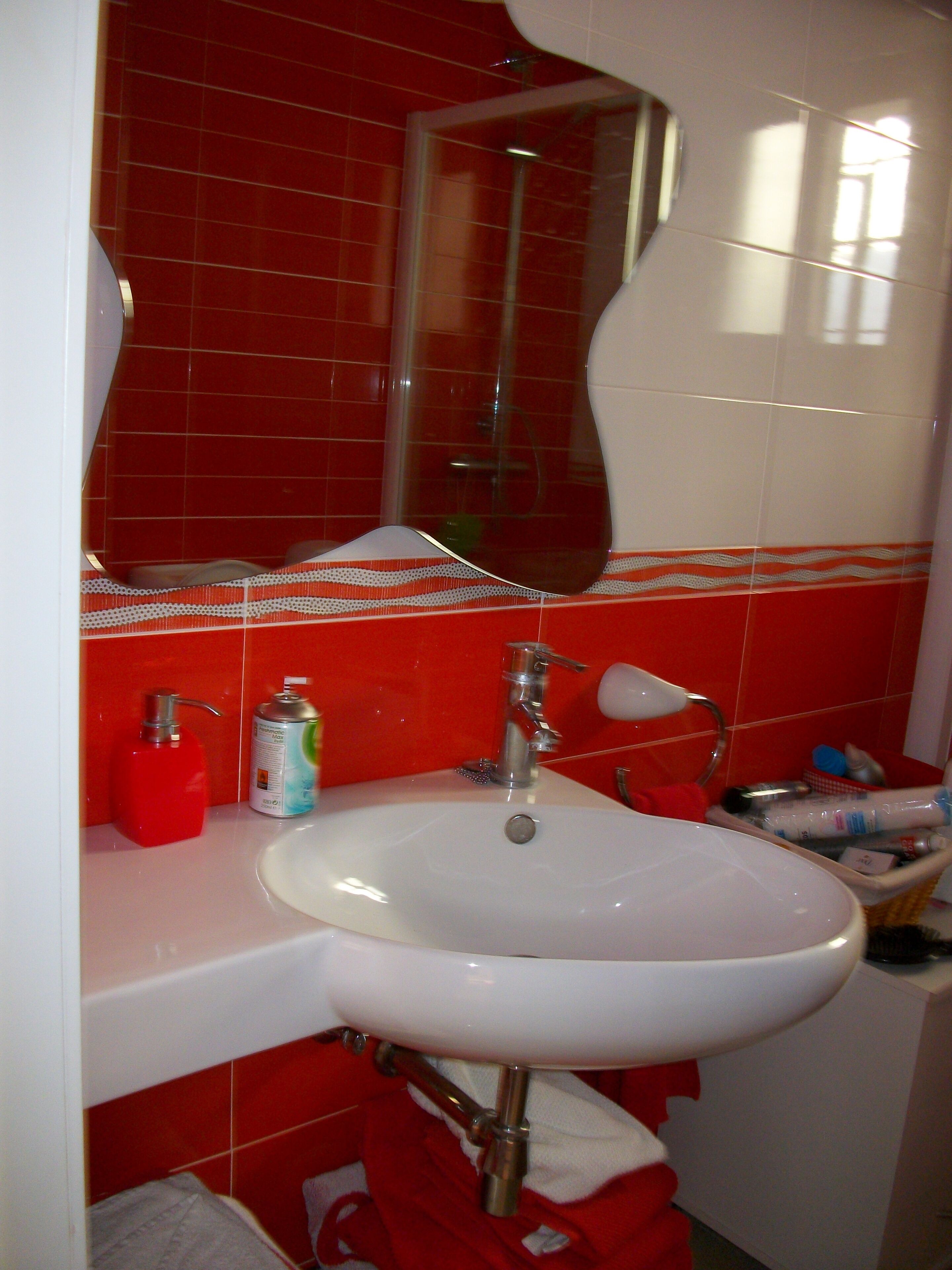Un baño con un lavabo blanco, baldosas rojas, un espejo y una toalla roja.