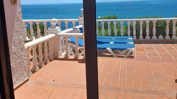 Un balcón con vista al mar, barandilla blanca y suelo de baldosas.