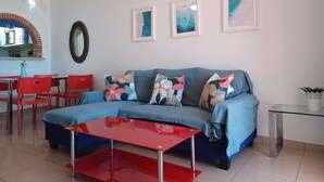 Una sala de estar moderna con un sofá azul, sillas rojas, una mesa de centro de vidrio y obras de arte enmarcadas en la pared.