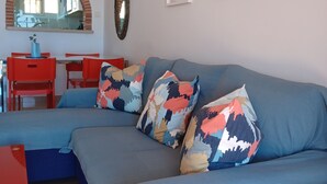 Una sala de estar moderna con un sofá azul, sillas rojas y una zona de comedor.