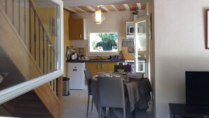 A compact kitchen with wooden beams, a dining area with a table and chairs, and a small refrigerator.