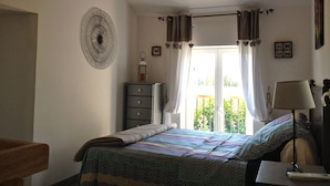 A bedroom with a bed, a dresser, a lamp, and a window with curtains.