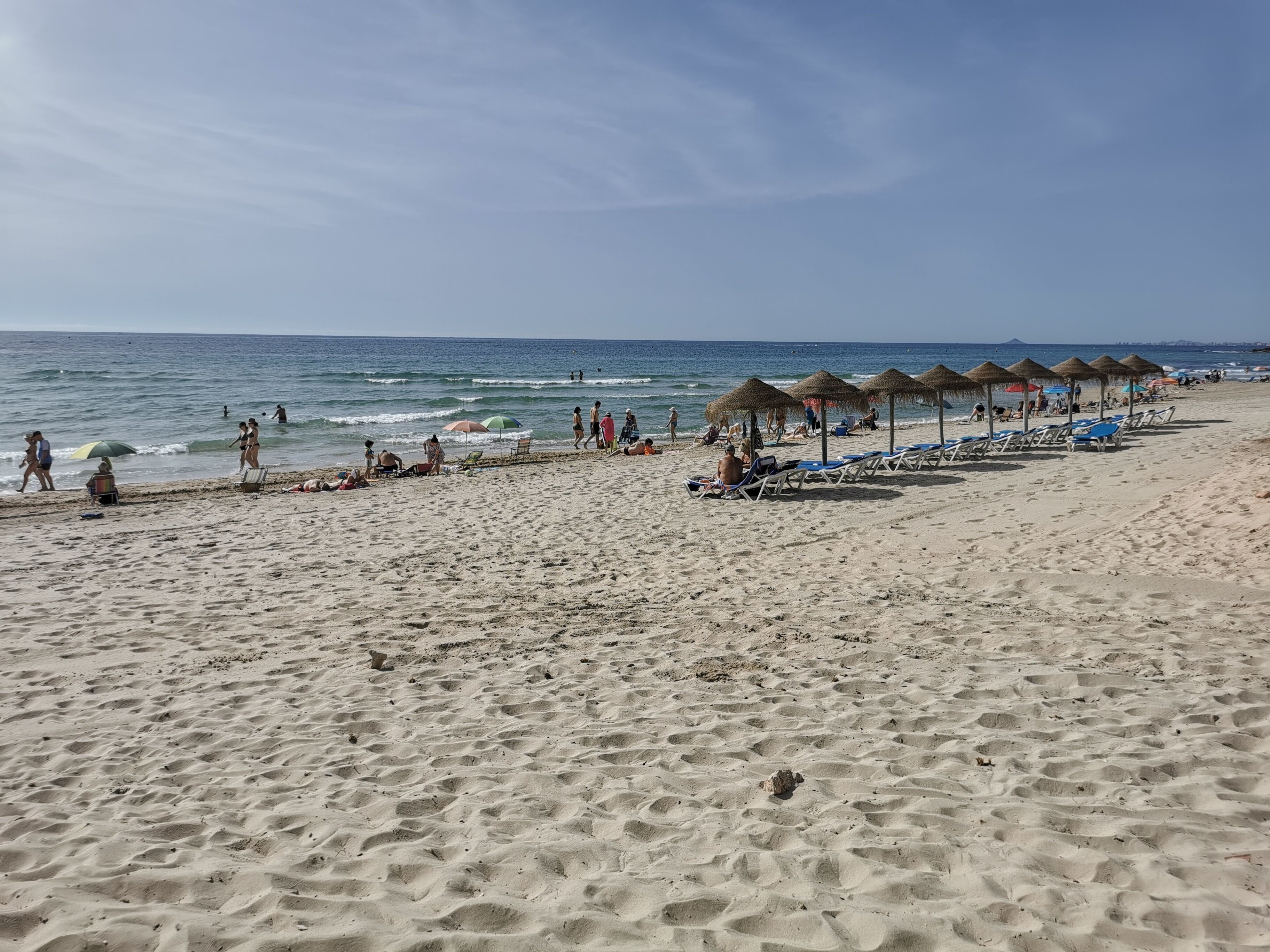 Una playa con filas de tumbonas y sombrillas, una orilla arenosa y el océano al fondo.