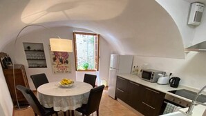 A compact kitchen with a dining area, featuring a round table, chairs, a refrigerator, a microwave, and a sink. - Historic House With Stunning Mountain Views in the heart of the village      (Pigna)
