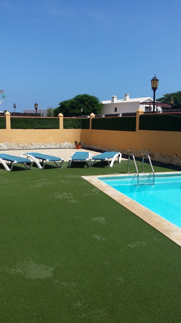 Un espace piscine agrémenté de gazon synthétique, d’une piscine et de chaises longues.