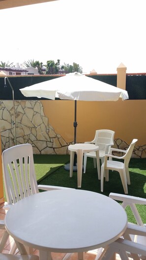 Une terrasse avec une table ronde et quatre chaises blanches, un parasol et un mur en pierre.