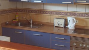 Una cocina con armarios azules, un lavamanos de acero inoxidable, un tostador y una tetera.
