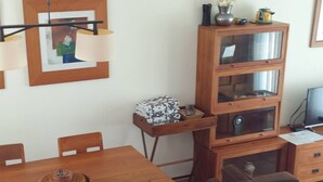 Un comedor con una mesa y sillas de madera, un sofá y un mueble bajo con puertas de vidrio.