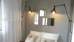A neatly made bed with a striped blanket, two bedside tables, a hanging lamp, and three wall-mounted mirrors. - duplex apartment 50m from the Arcachon Basin (Lège-Cap-Ferret)