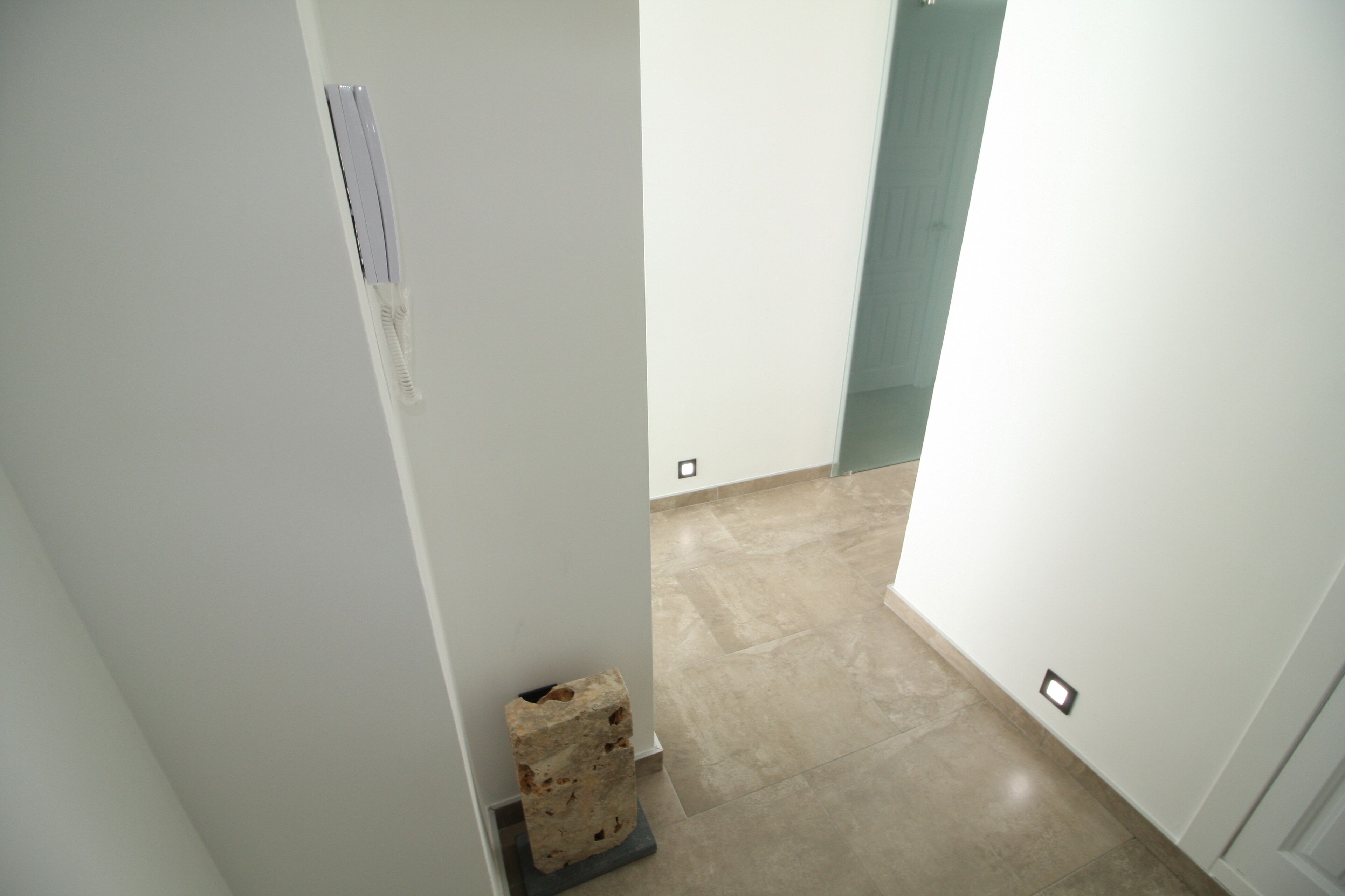 Ein schmaler Flur mit weißer Wand, Stein Sockel und Fliesenboden.