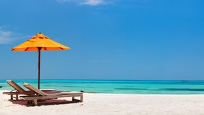 Une plage avec une chaise longue en bois et un parasol orange.