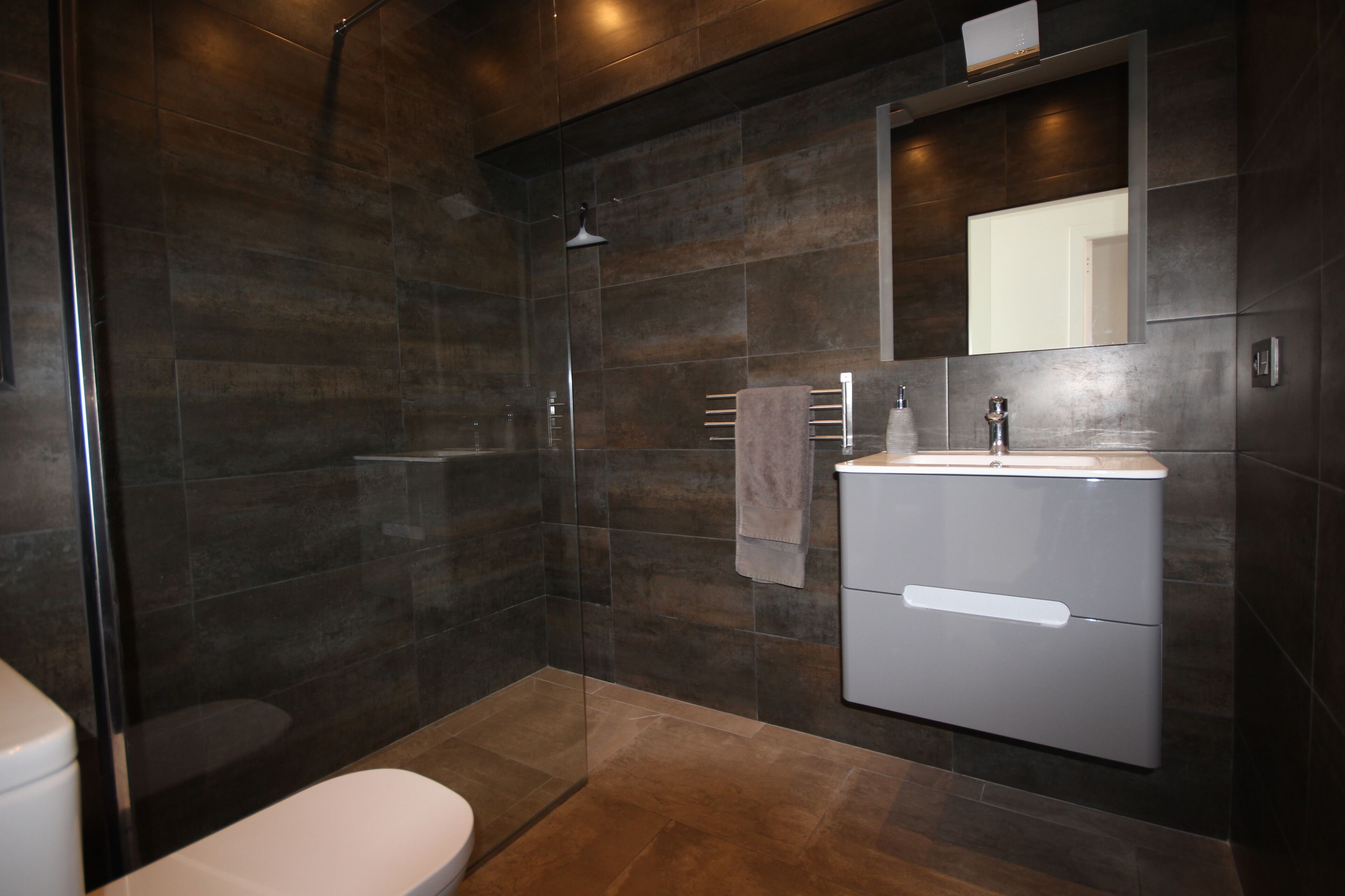 A modern bathroom with a glass shower enclosure, a white toilet, and a built-in sink with a mirror above it.