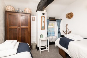 A bedroom with two beds, a wooden wardrobe, a small table, and a window with curtains. - Stunning house right by the sea, spectacular far reaching sea views in Polperro (Polperro, Cornwall)