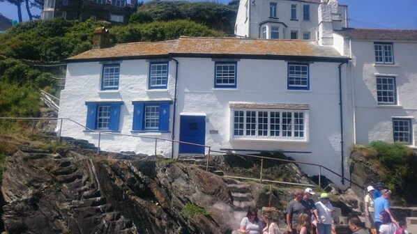 A white building with blue shutters and a blue door, located near rocky terrain. - Stunning house right by the sea, spectacular far reaching sea views in Polperro (Polperro, Cornwall)