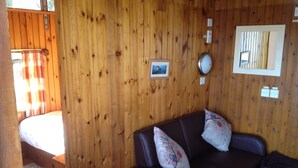 A wooden interior with a bed, a dark brown sofa with floral cushions, and a small framed picture on the wall.