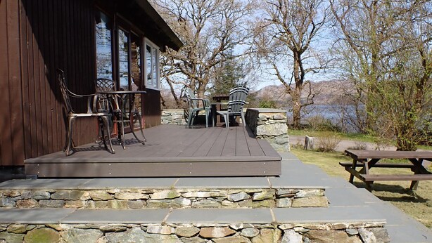 A wooden building with a stone staircase leading to a deck with outdoor furniture.