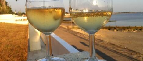 Two wine glasses on a stone ledge by a beach.