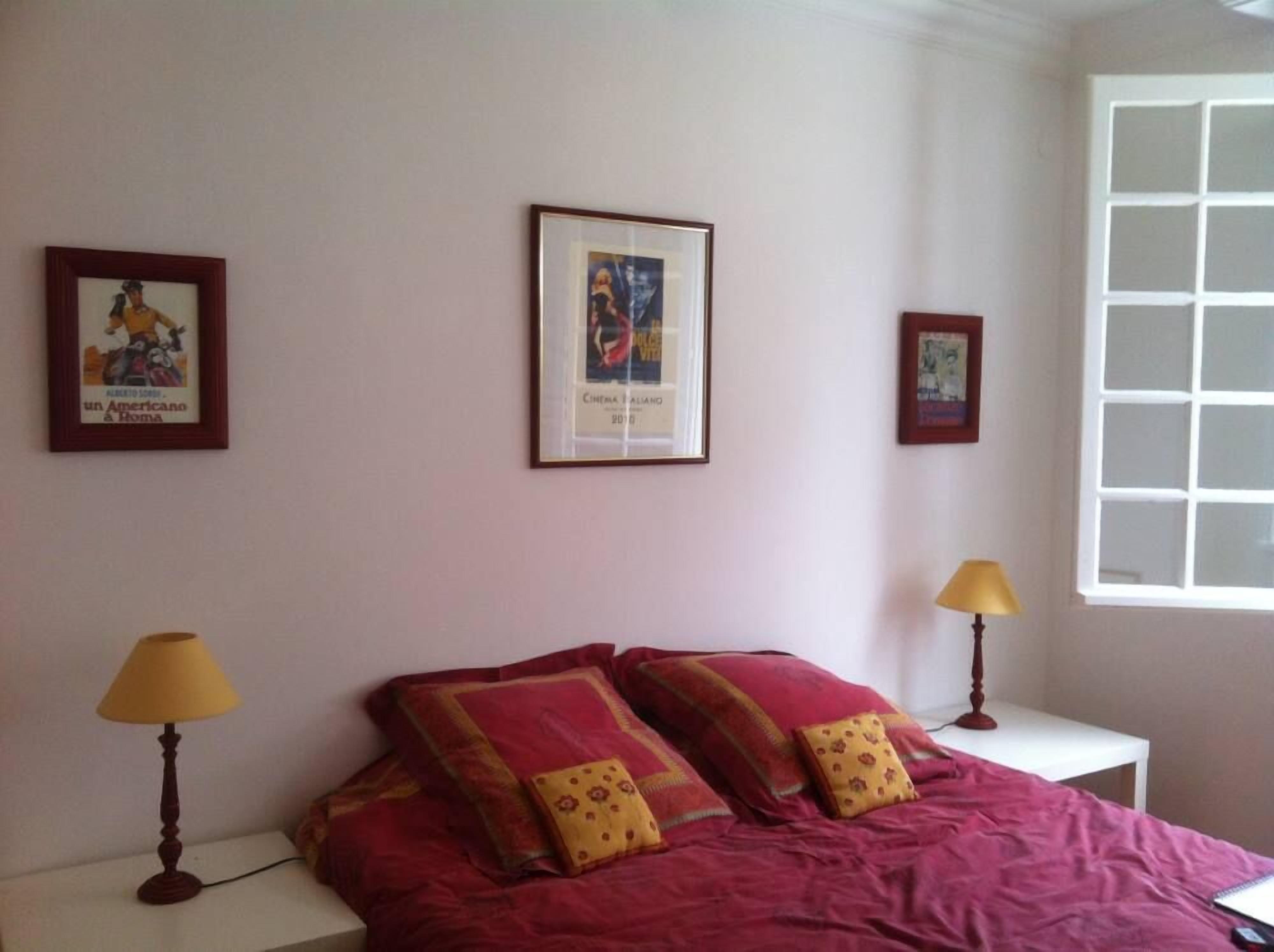 Une chambre à coucher avec un lit, deux lampes de chevet et trois tableaux encadrés accrochés au mur.