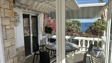 Relax on the balcony overlooking the sea and lush greenery, with a glass door leading to a scenic view.