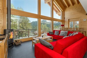 L’intérieur chaleureux d’un chalet en bois, avec un canapé rouge, une cheminée et de grandes fenêtres donnant sur la forêt.