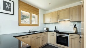 A modern kitchen with wooden cabinets, a black countertop, a built-in oven, and a window with a view of a building. - Chalet Anna - La Tzoumaz, 4 Vallees (La Tzoumaz)