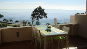 A terrace with a table and chairs, overlooking a beach and the sea. - Bahia Beach Front Apartment - Close to Marbella - Free WiFi (Estepona)