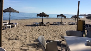 A beachside restaurant with outdoor seating, including tables and chairs, and thatched umbrellas providing shade. - Bahia Beach Front Apartment - Close to Marbella - Free WiFi (Estepona)