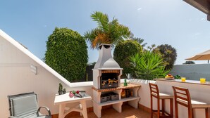 Un patio al aire libre con una parrilla, asientos y una pequeña mesa con bebidas.