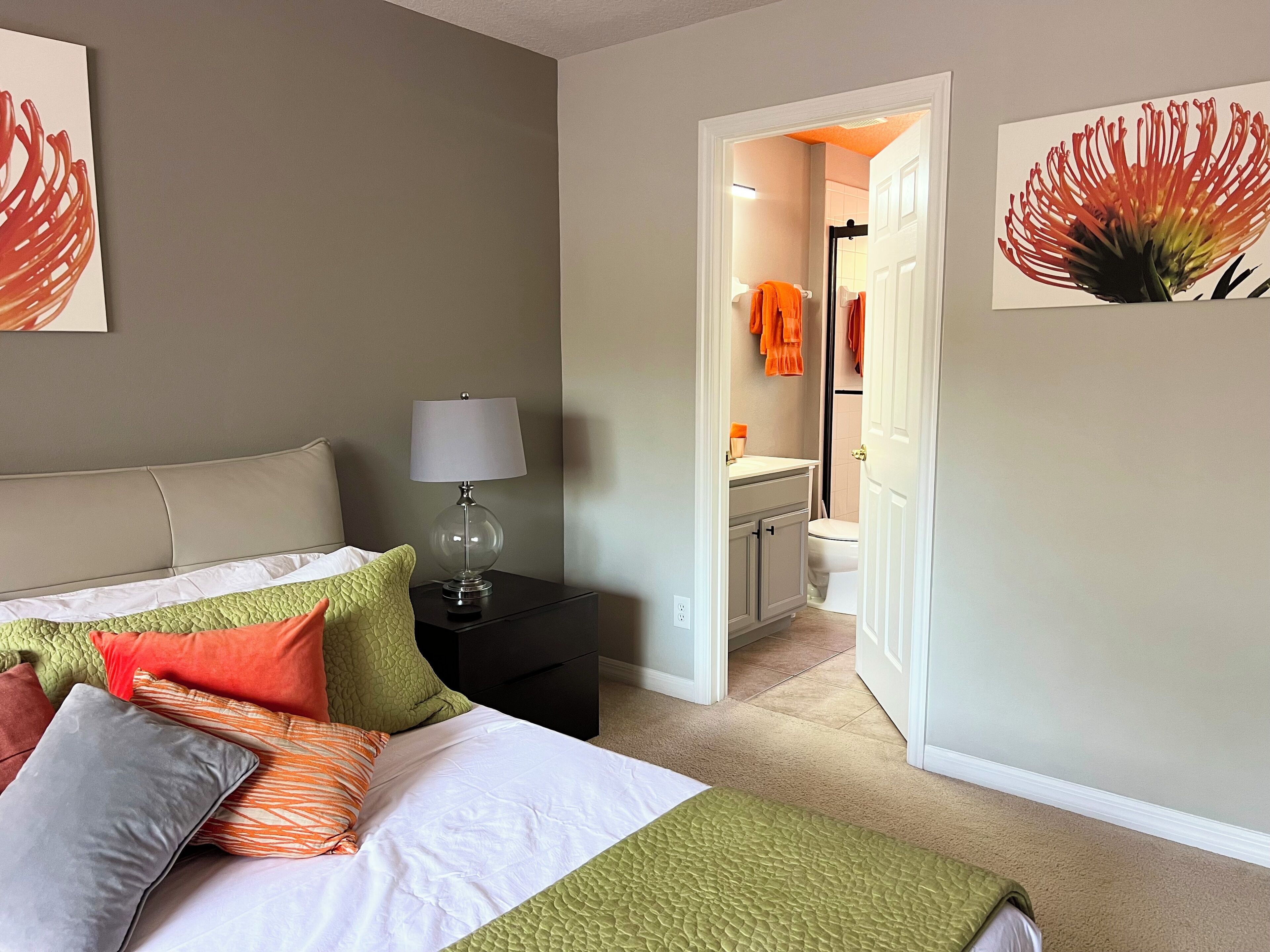 Een slaapkamer met een bed, nachtkastje, lamp en uitzicht op de badkamer.