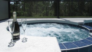 Un bain à remous avec une bouteille de champagne et un verre posés sur une table, le tout entouré d’un paysage arboré.