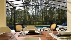 Un coin repas offrant une vue sur une piscine et des arbres, avec une table mise avec des assiettes, des verres et des couverts.
