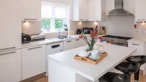 A modern kitchen with white cabinets, a stainless steel range hood, a built-in oven, and a window providing natural light. - New Forest cottage, sleeps up to 10. Looks directly on to the Forest  (Brockenhurst)