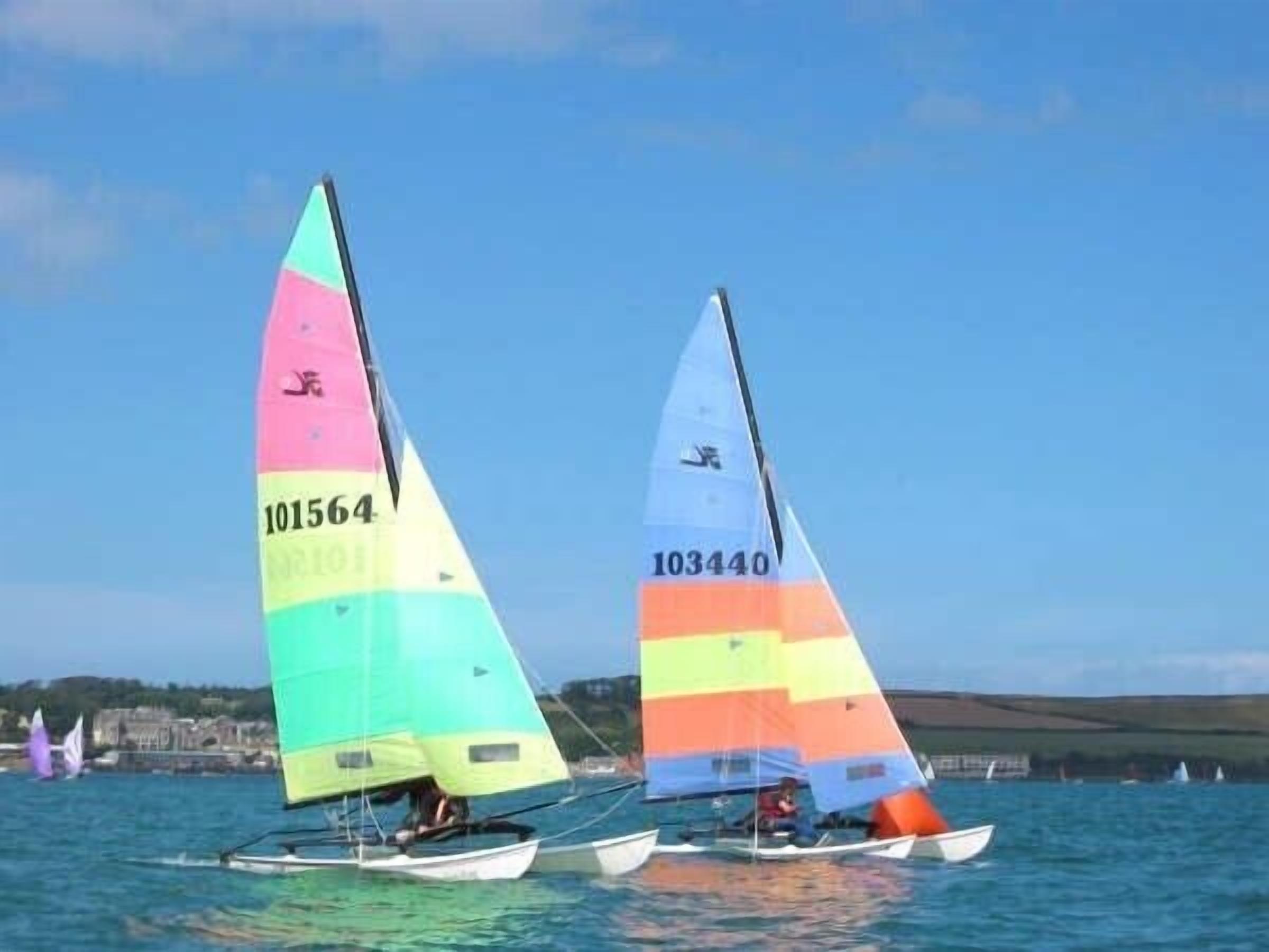Two sailboats with colorful sails on a body of water.