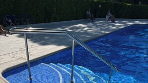 Una piscina con agua azul cristalina, borde de azulejos y baranda metálica.