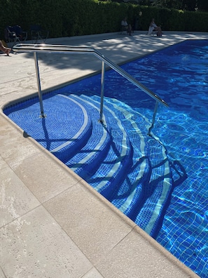 Una piscina con agua azul cristalina, borde de azulejos y baranda metálica.