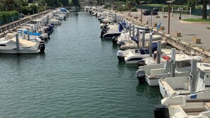 Una marina con barcos amarrados a lo largo de un canal, rodeada de vegetación y un cielo despejado.