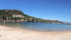 Una playa con gente tomando el sol y nadando, un litoral rocoso y edificios al fondo.