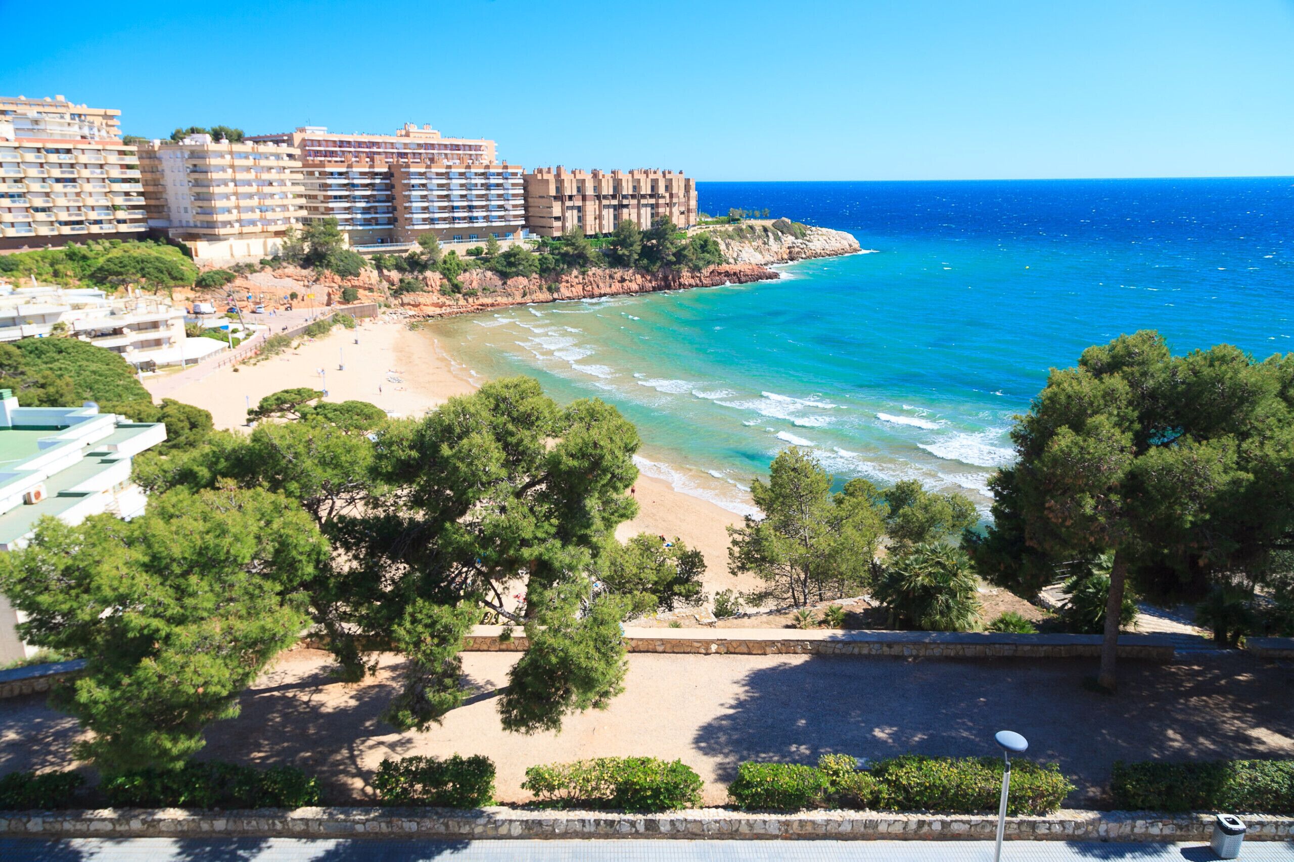 A coastal hotel with multiple buildings, a beach, and a rocky shoreline.
