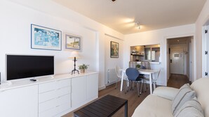 Una sala de estar moderna con televisor de pantalla plana, un sofá, una mesa de centro y un comedor con una mesa y sillas.