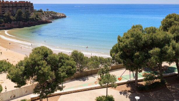 Vista costera con playa, un edificio y árboles.