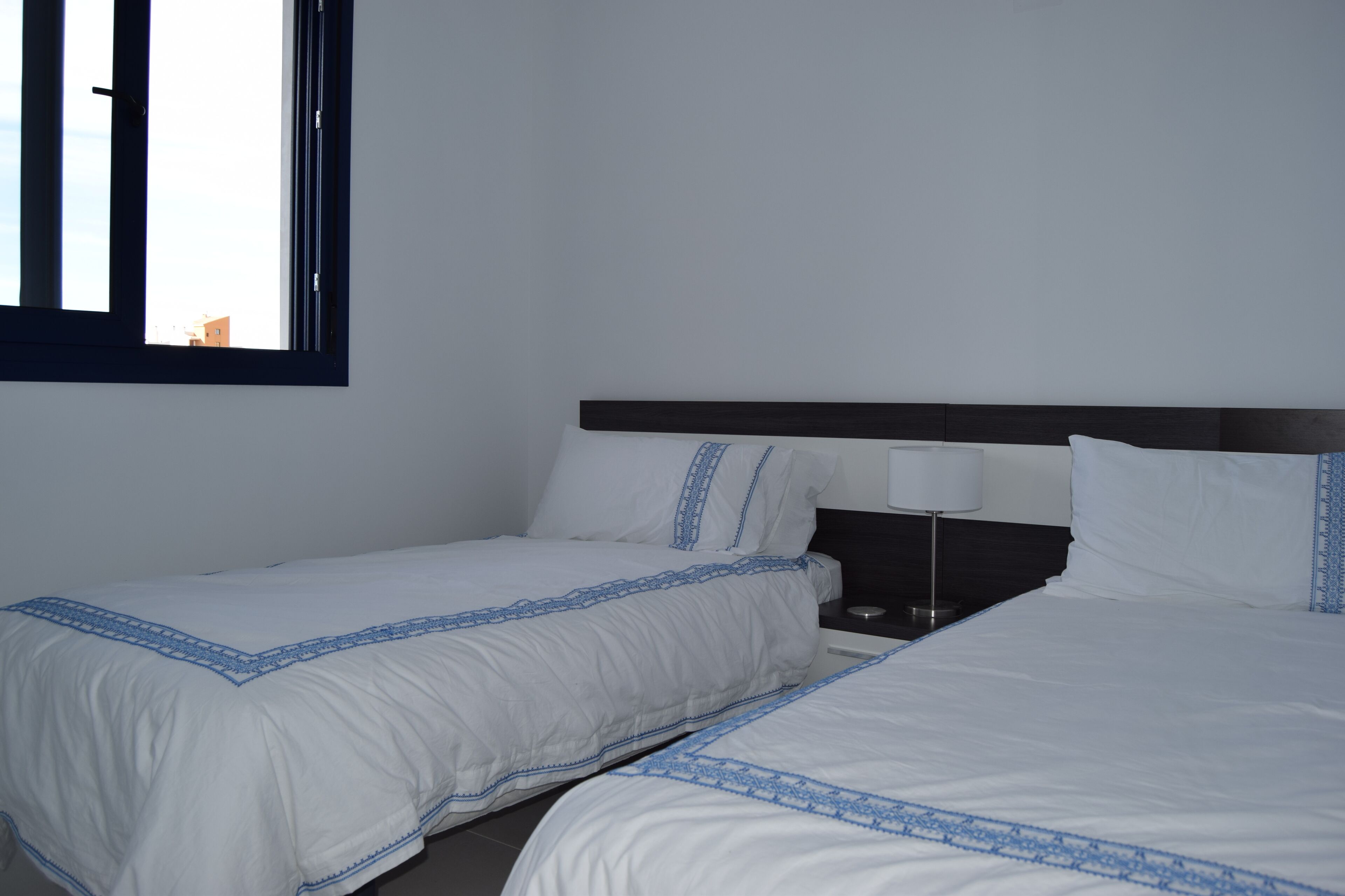 A hotel room with two single beds, a nightstand with a lamp, and a window with blinds.
