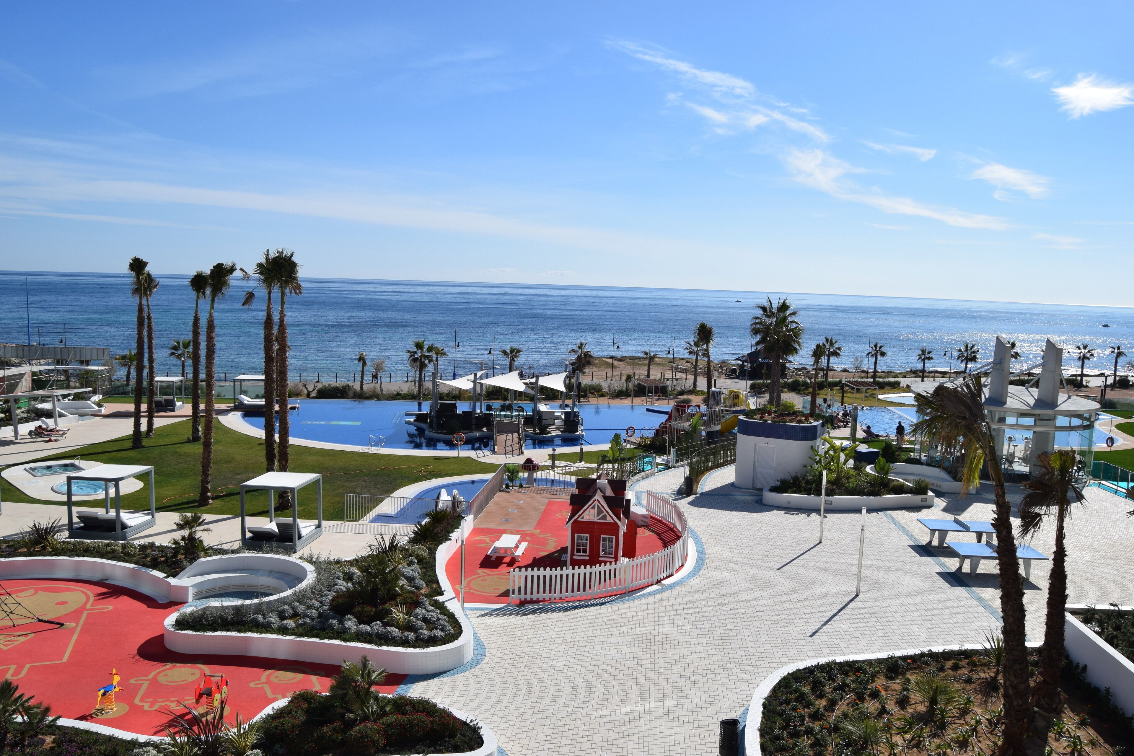 A resort with a pool area, palm trees, and a view of the ocean.
