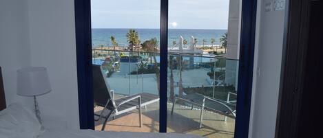 A hotel room with a balcony overlooking a pool and beach.