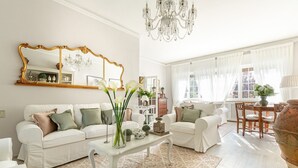 Amplia sala de estar con dos sofás blancos, una mesa de centro y un candelabro.
