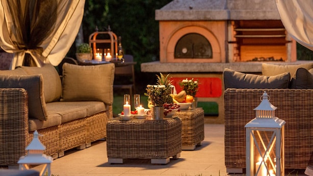 Un área de estar al aire libre con mobiliario de mimbre, velas y una cesta de frutas.