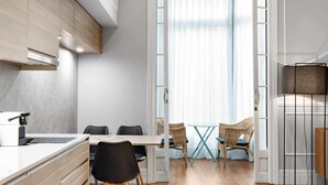 Una cucina moderna con mobili in legno, un piano di lavoro bianco e un'area pranzo con sedie in vimini e un tavolo in vetro.