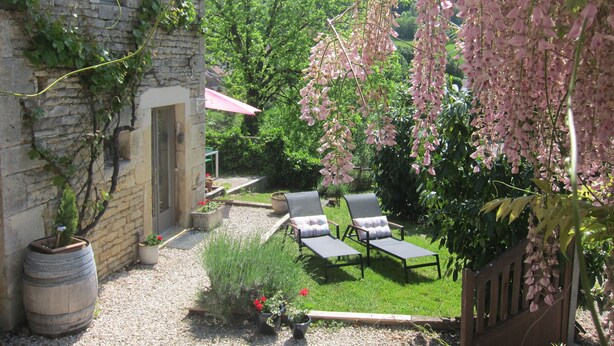 A stone building with a small window, a gravel patio, two lounge chairs, and a hanging pink flower display. - Picturesque. A modern barn conversion, sleeps 5. Stunning views. (Frôlois)