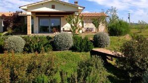 Ein Haus mit Ziegeldach, einer Terrasse mit Gartenmöbeln und einem Garten mit verschiedenen Sträuchern.