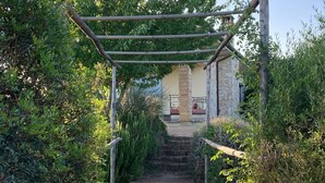 Ein Holzweg führt zu einem Steinhaus mit einer Pergola darüber.