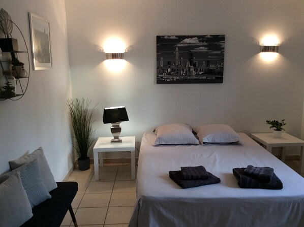 Une chambre à coucher bien rangée, avec un lit, deux tables de chevet, une lampe et un tableau représentant un paysage urbain accroché au mur.
